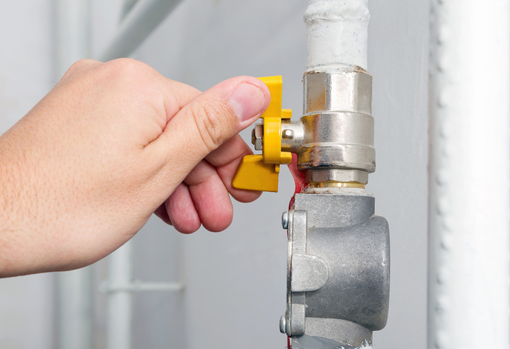 Person's hand opens or closes yellow gas valve on gas pipe at home. Symbolic image of natural gas savings in the heating season. Part of body, selective focus.